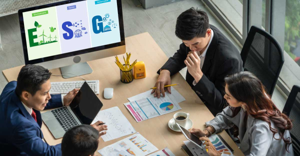 Three people in a business meeting, discussing data on a computer screen; faces are blurred for privacy.