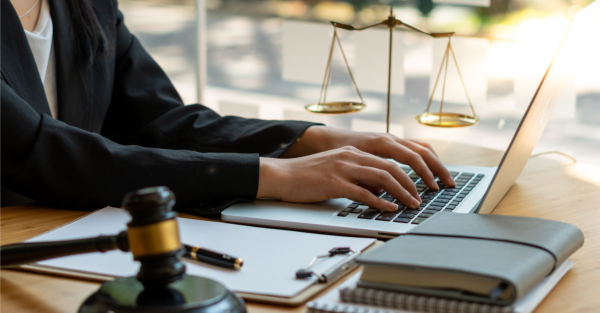Lawyer typing on a laptop with scales of justice in the background.