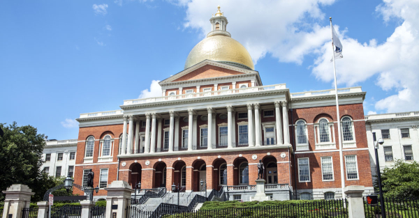 The Massachusetts state capitol building shown at a slight angle, with a white flag flying in front of it.