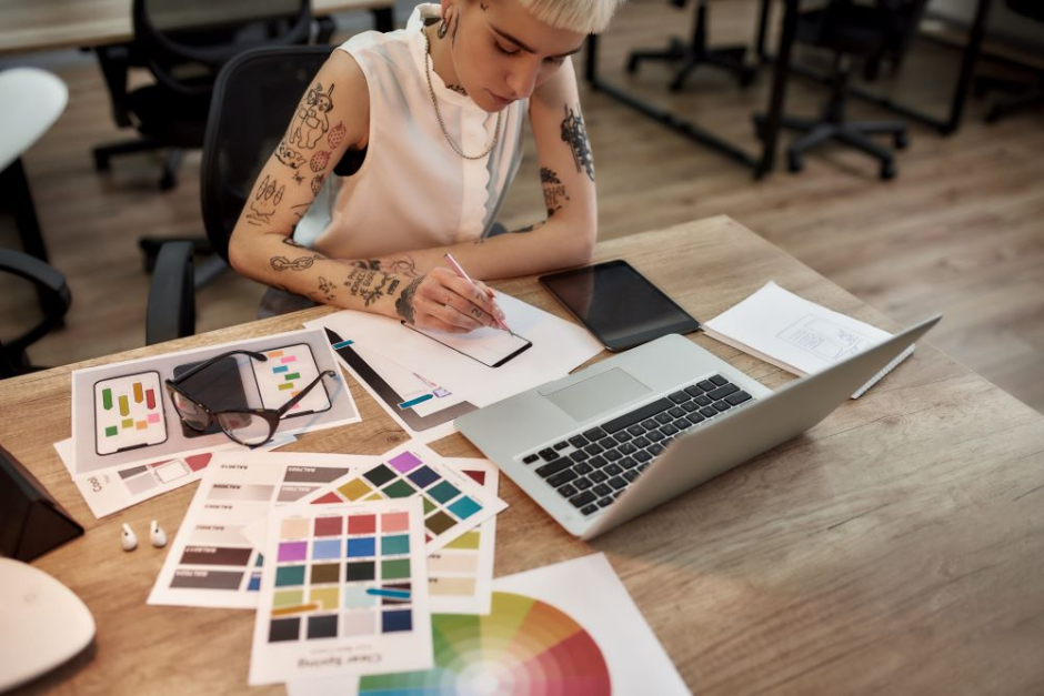 A woman with tattoos working at a desk with a laptop.