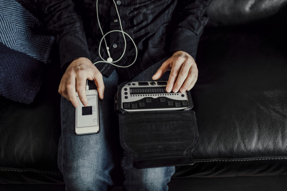 A person sitting on a couch interacting with a smartphone using a screenreader and headphones.