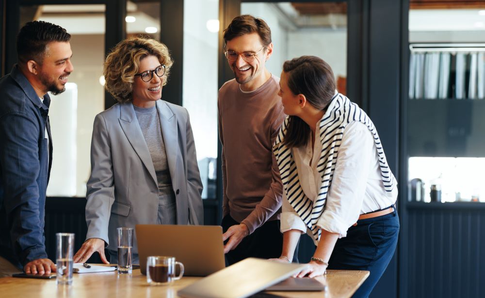 A group of smiling coworkers gather around the edge of a conference room table.