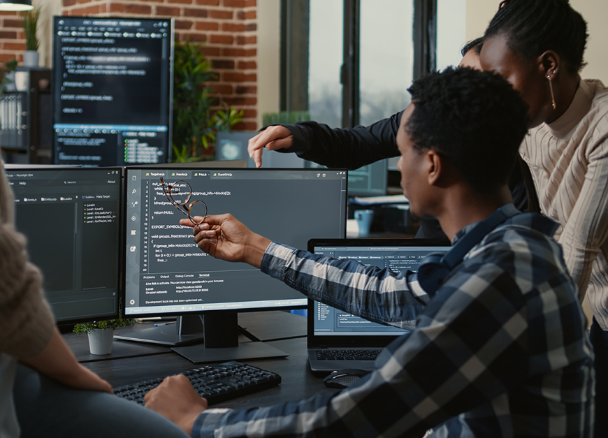 Group of people around a desk troubleshooting computer code on the monitor.